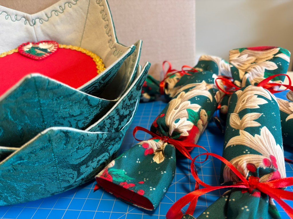 A collection of decorative fabric items, including a turquoise basket with a red lining featuring a holiday motif, and several green and cream Christmas crackers tied with red ribbons.